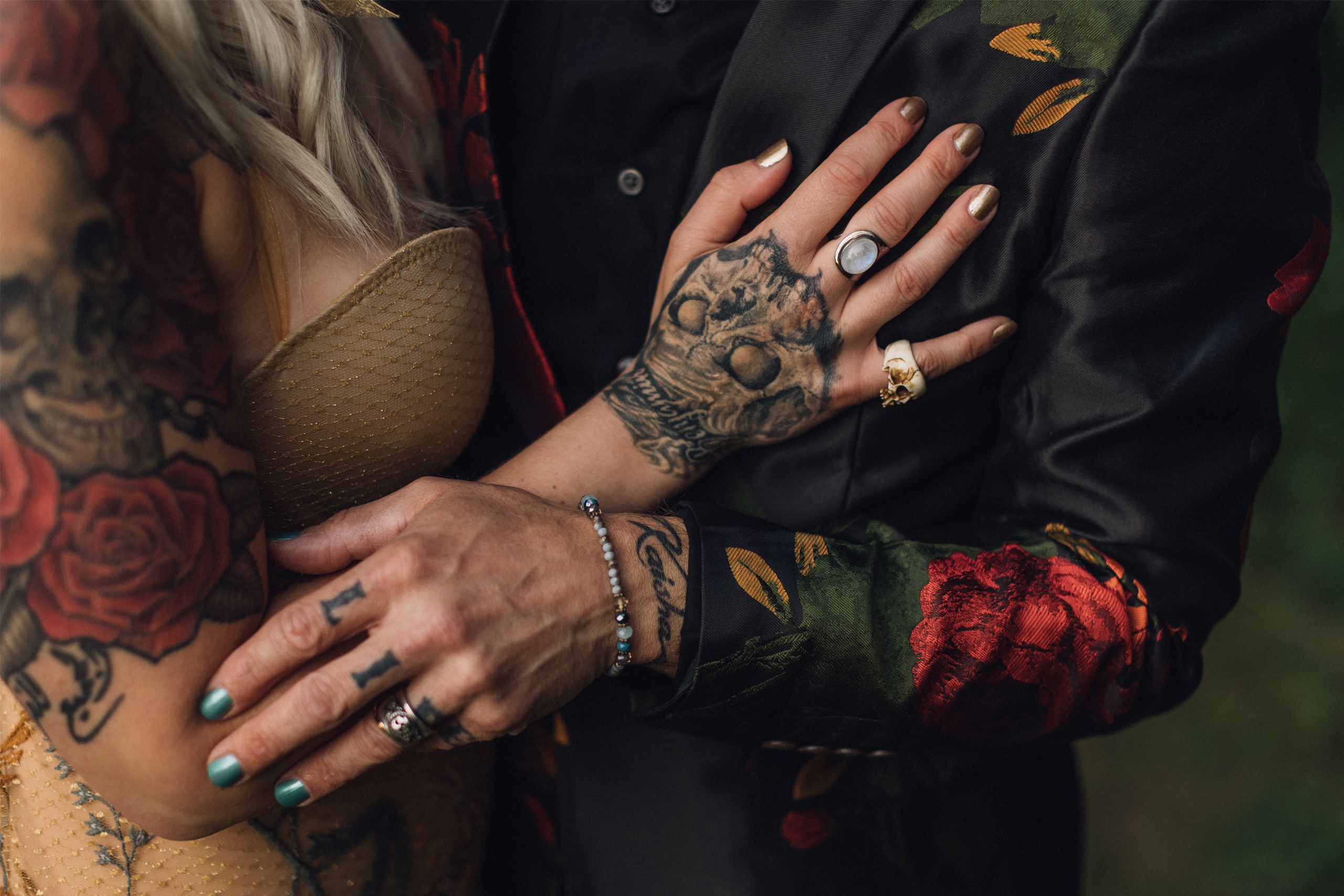 A tattoo artist couple embraces after getting married. A close up of their tattooed hands with their wedding rings.